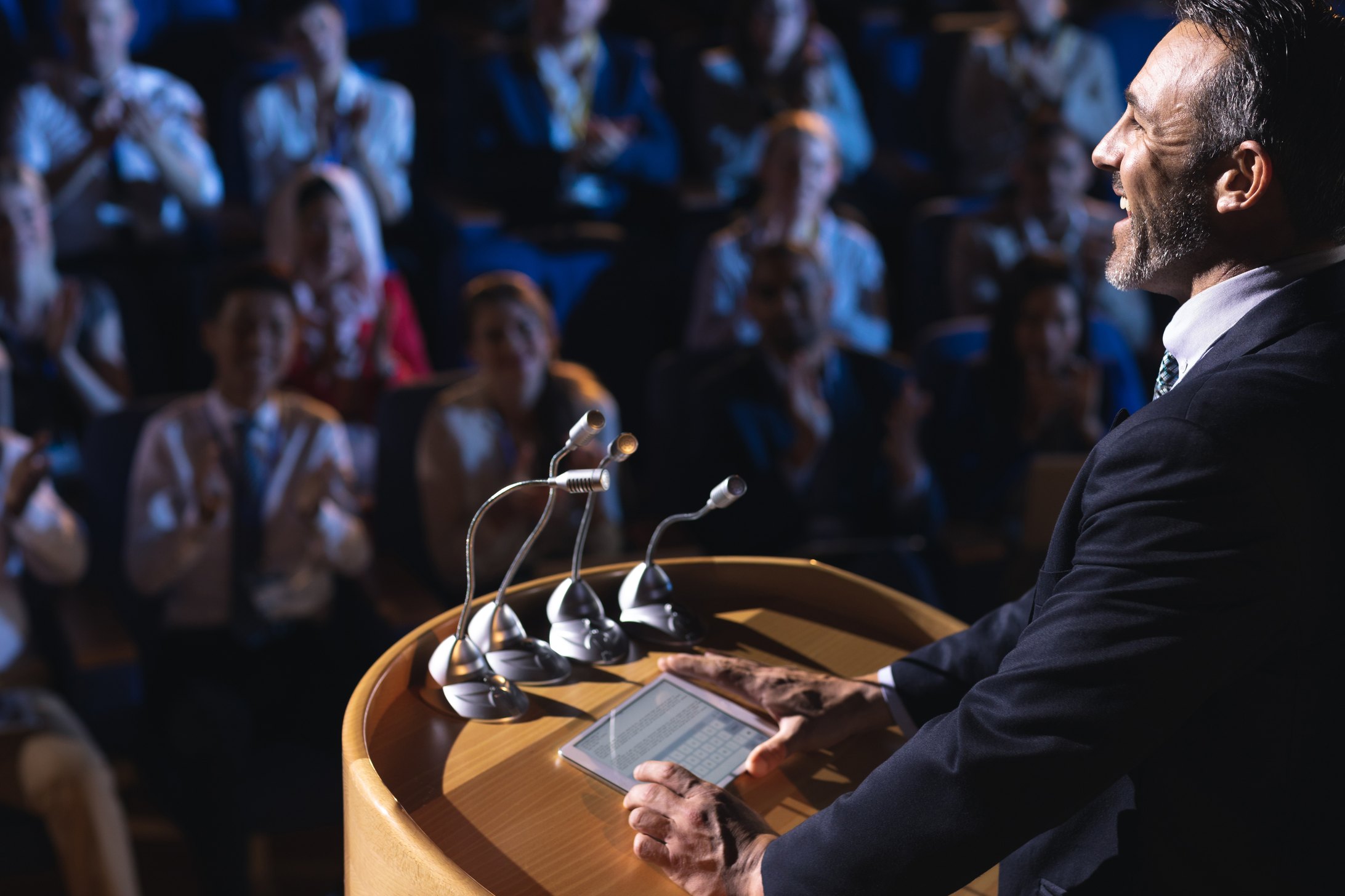 A speaker at a lectern addressing an applauding audience at a conference